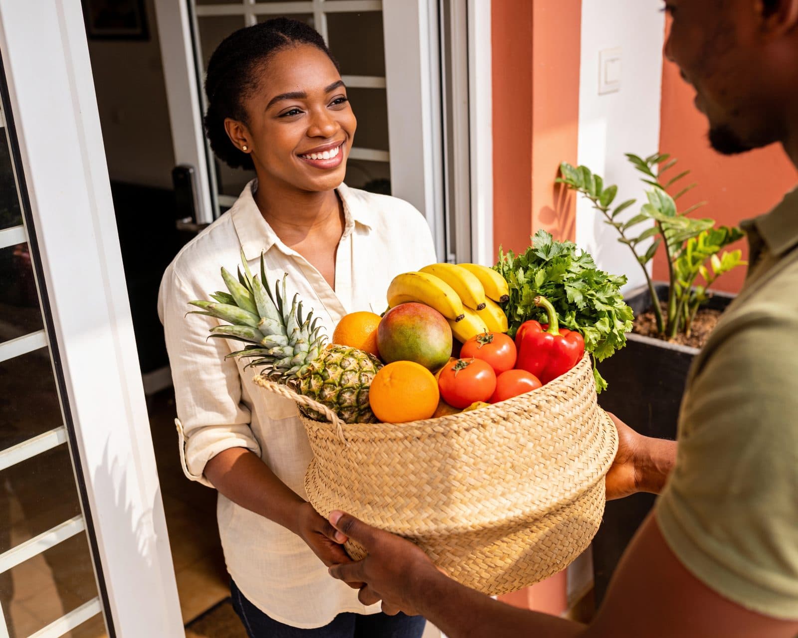 A rider hands a basket of fresh fruit and vegetables to a woman at her front door