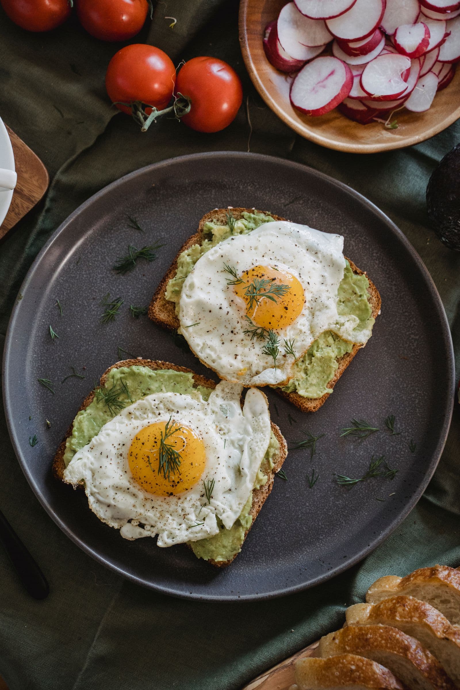 Two slices of toast topped with avocado and a fried egg on a dark plate