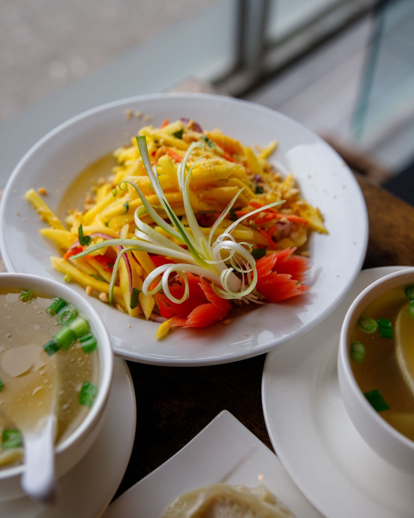Shredded green mango and carrot salad with tomato and spring onion on a white plate