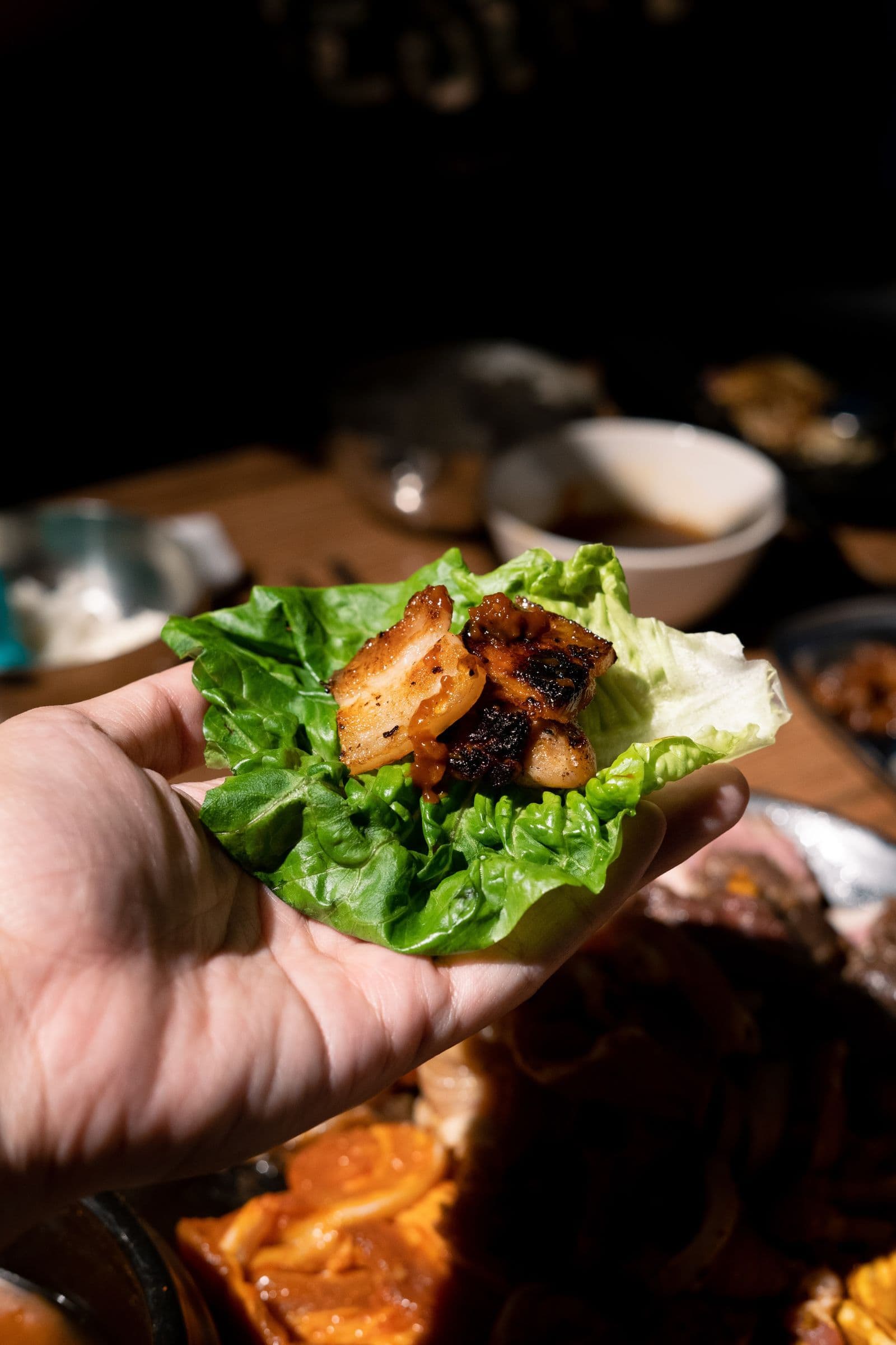 A hand holding a crisp lettuce leaf wrapped around grilled meat