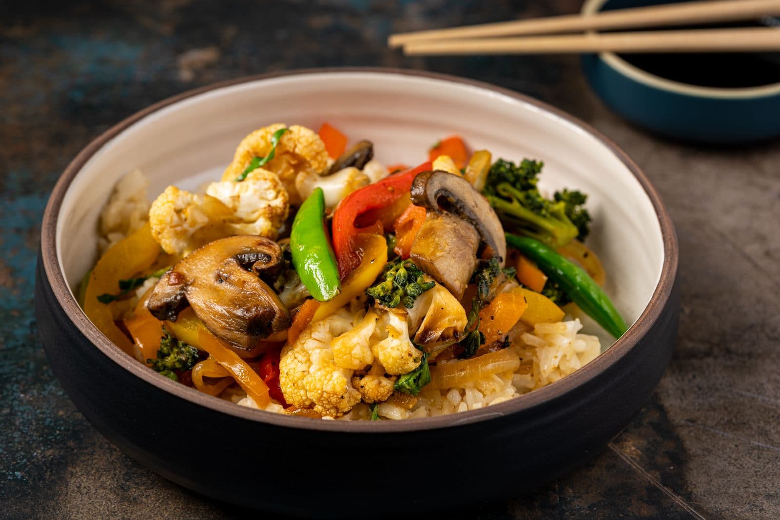 A bowl of stir-fried mushrooms, peppers and cauliflower with chopsticks
