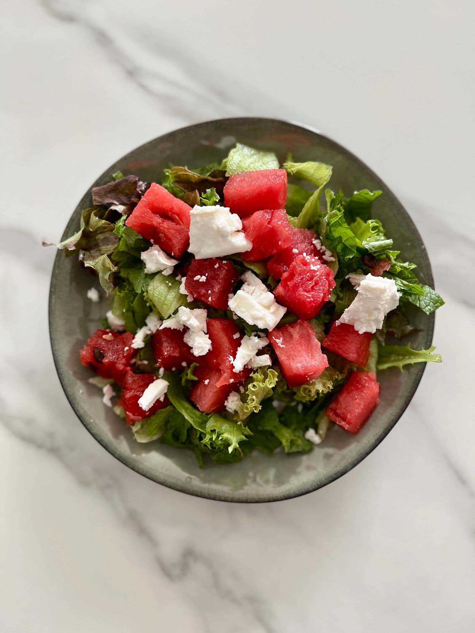 Cubes of watermelon and white cheese over salad leaves in a grey bowl